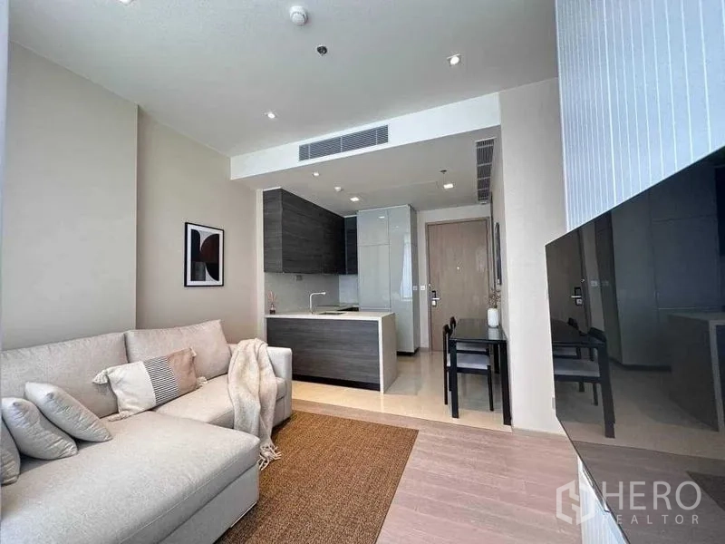 Condominium for rent in Watthana, Bangkok - Bright living area with sectional sofa, TV wall and compact kitchen