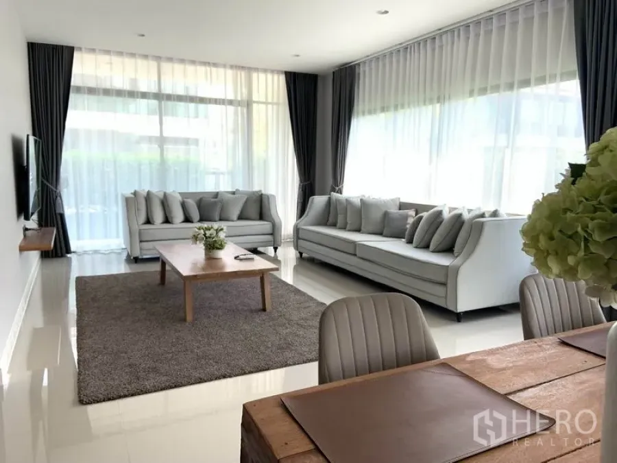 บ้าน ให้เช่าหรือขายในBang Kapi, Bangkok - ห้องนั่งเล่นสว่างด้วยหน้าต่างเต็มบาน โซฟาสีเทาสองตัวและมุมทานอาหาร