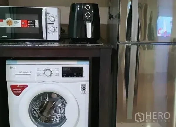 Condominium for rent in Huai Khwang, Bangkok - Appliance nook showing microwave, air fryer, front-load washer and stainless-steel refrigerator.