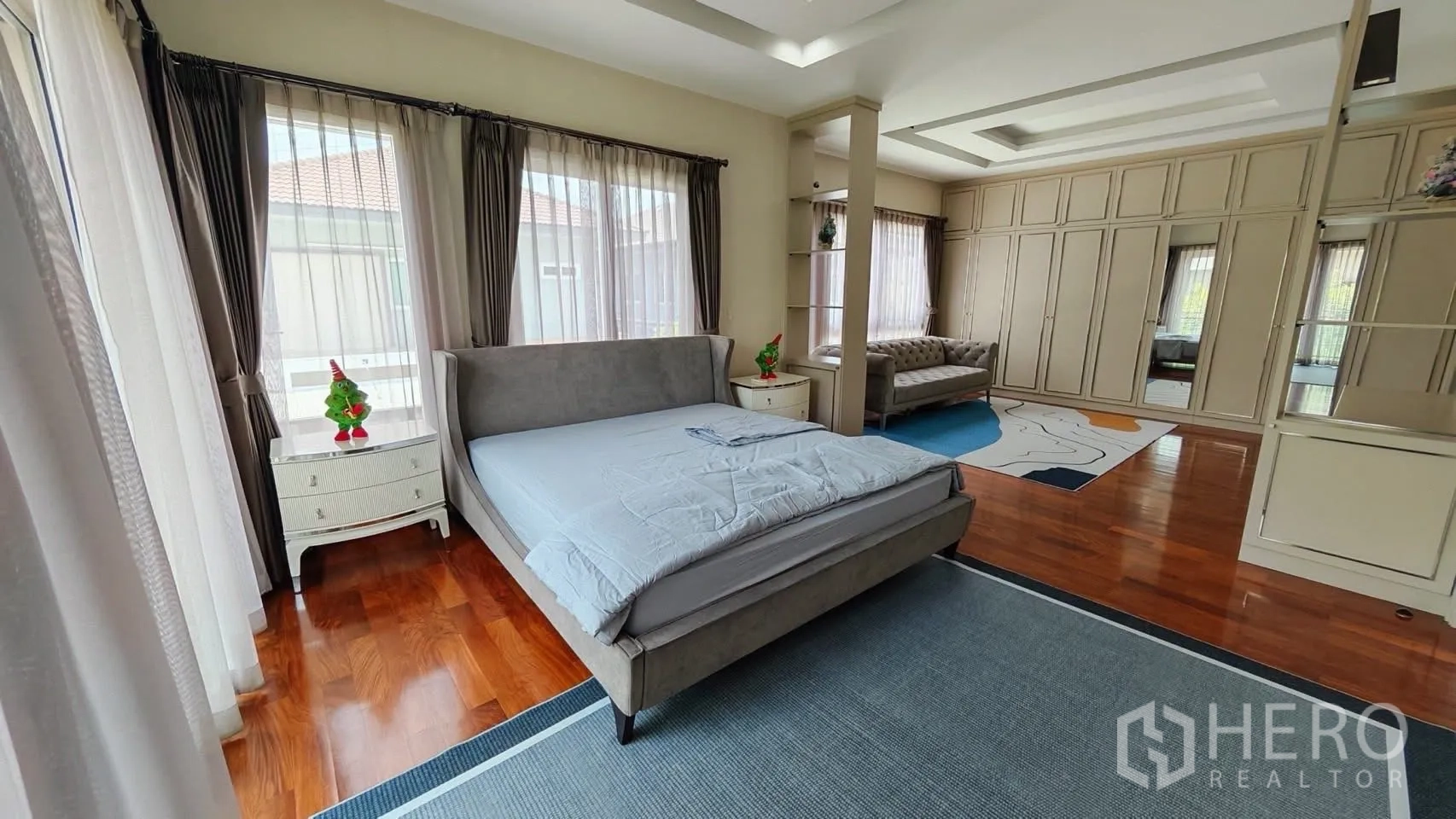 Detached House for rent or sale in Bang Phli, Samut Prakan - Master bedroom with wide windows, grey bed frame, and an adjacent lounge area.