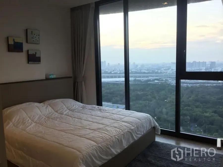 Condominium for rent in Chatuchak, Bangkok - Bedroom with floor-to-ceiling windows offering park and city skyline views.