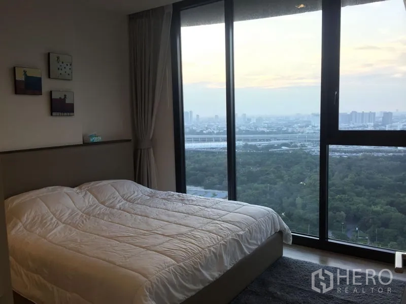 Condominium for rent in Chatuchak, Bangkok - Bedroom with floor-to-ceiling windows offering park and city skyline views.