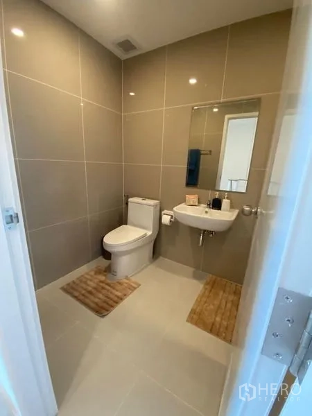 Townhouse for rent in Bang Kapi, Bangkok - Modern bathroom with beige tiles, toilet, basin, and wall mirror.