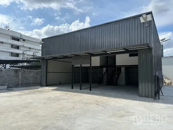 Warehouse for rent - Modern warehouse exterior with wide covered loading bay and a large paved yard under blue sky.