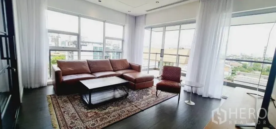 คอนโด ให้เช่าในWatthana, Bangkok - ห้องนั่งเล่นมุมกระจกเต็มบาน โซฟาหนัง พรมลาย และวิวเมือง