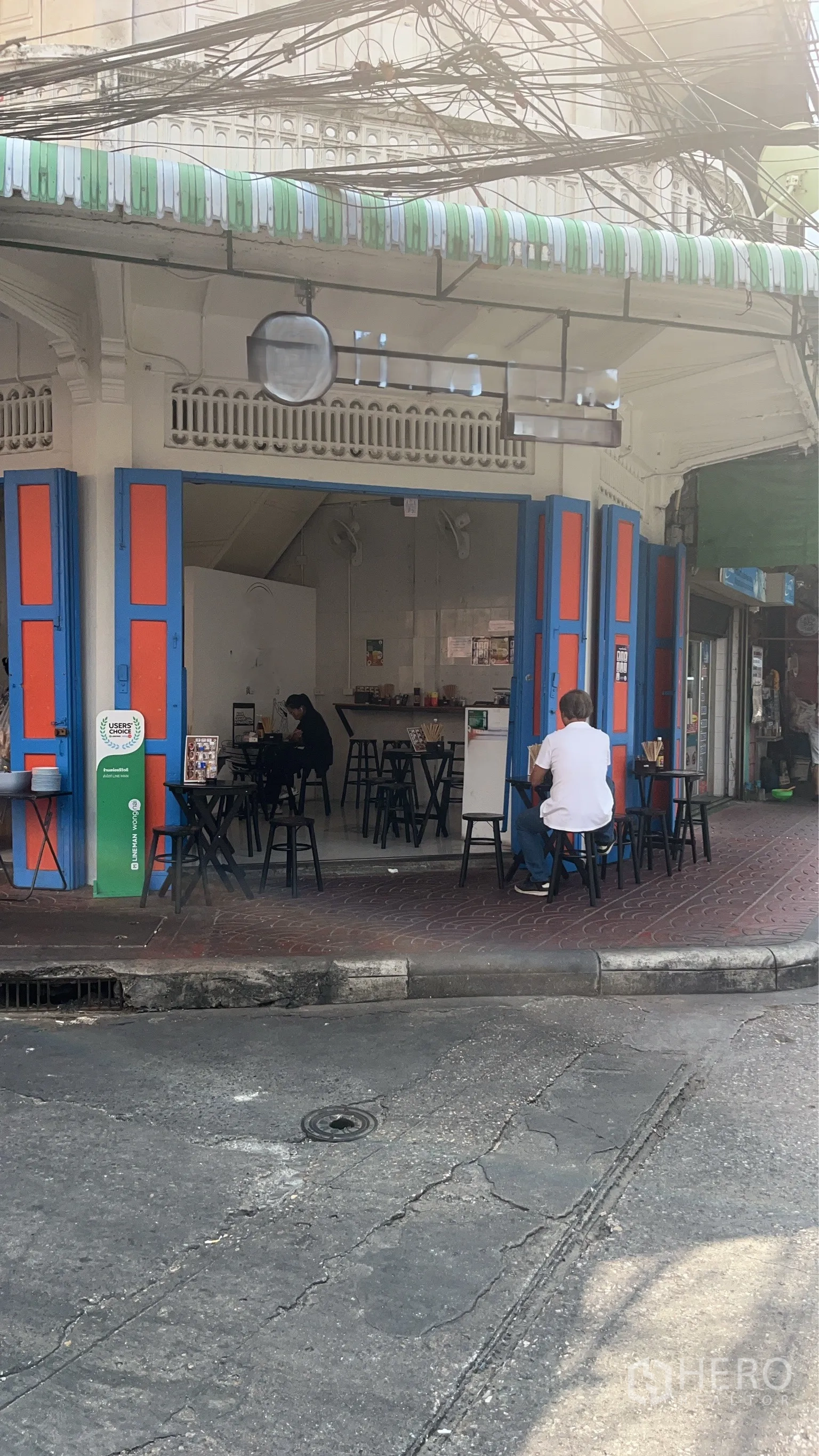 零售空间 for rent in Samphanthawong, Bangkok - 转角商铺，蓝橙色折叠门与条纹遮阳篷，门前可外摆，店内可见开放式吧台。