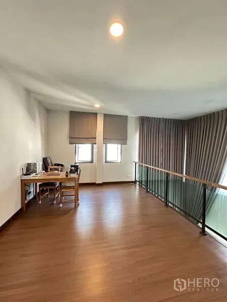 独立式住宅 出租在Bang Phli, Samut Prakan - 夹层书房区，木地板、书桌与俯瞰客厅的玻璃扶手。