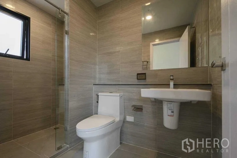 Detached House for rent in Khlong Sam Wa, Bangkok - Modern gray-tiled bathroom with glass shower, toilet and wall-mounted sink