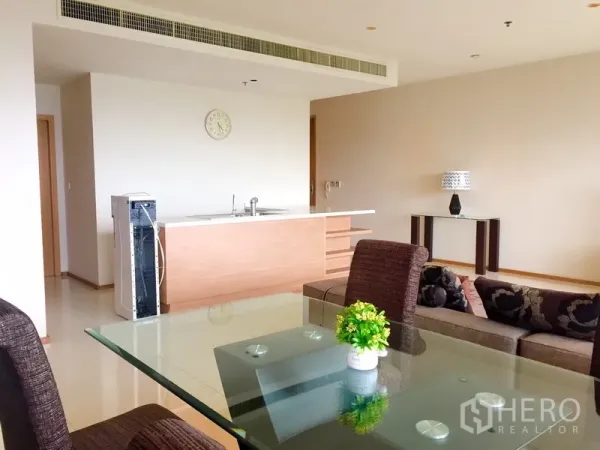 คอนโด ให้เช่าในKhlong Toei, Bangkok - พื้นที่นั่งเล่นแบบโอเพ่นแปลน โต๊ะอาหารกระจก เก้าอี้สีน้ำตาล โซฟา และไอส์แลนด์ครัวสไตล์มินิมอลพร้อมแอร์ฝังฝ้า