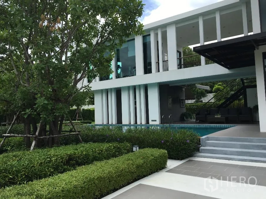 Detached House for rent or sale in Bang Na, Bangkok - Swimming pool beside a contemporary clubhouse with shaded seating and landscaped gardens.
