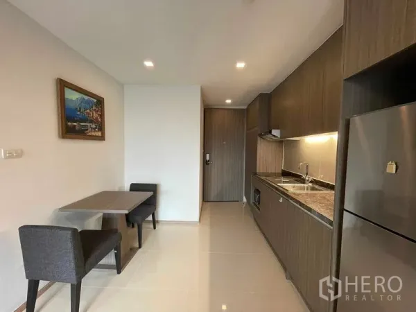 公寓 出租在Watthana, Bangkok - 紧凑餐区与长形橱柜式厨房相邻，尽头为入户门。