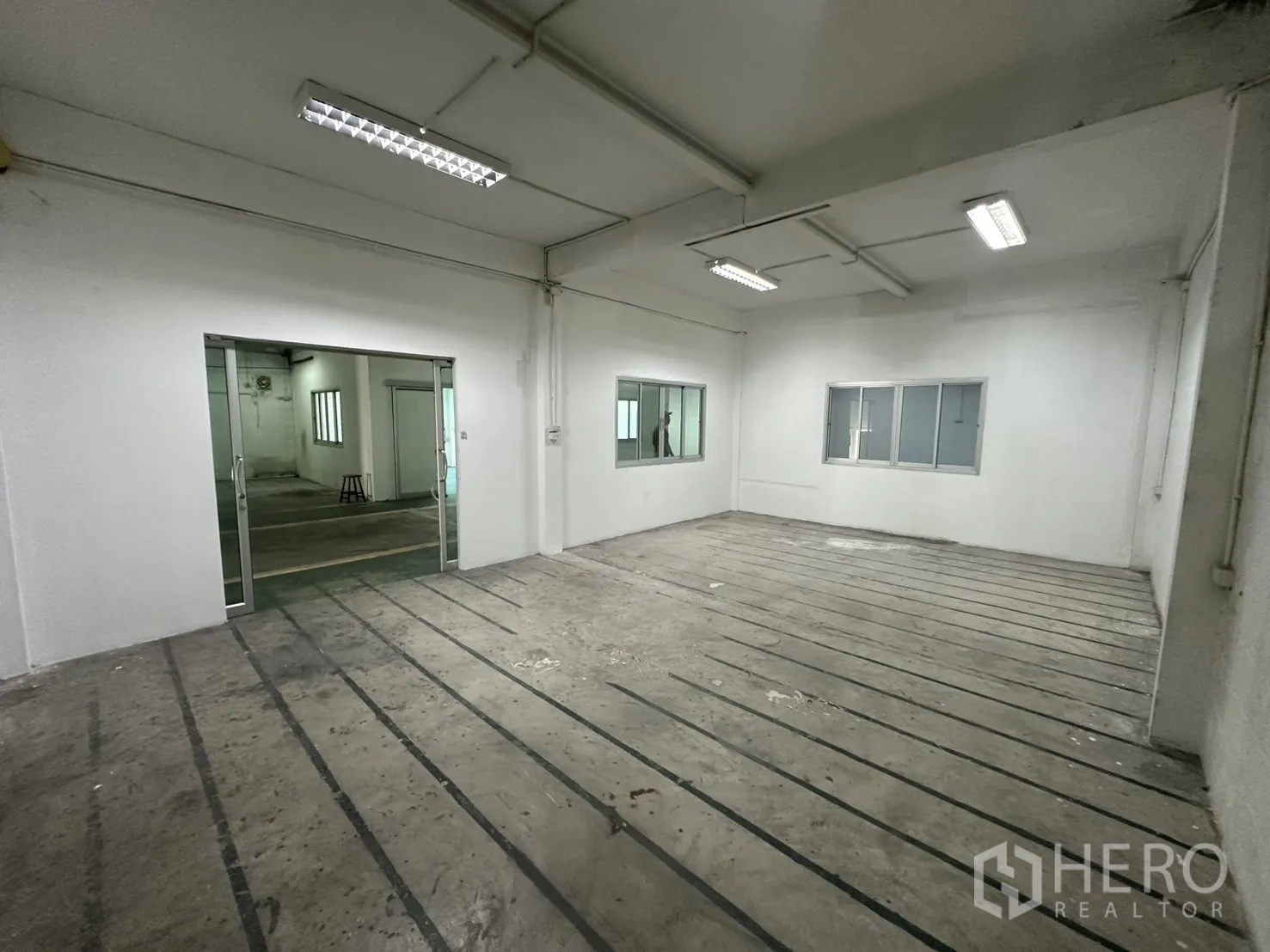 Warehouse for rent in Bang Na, Bangkok - Large production room with strip-marked concrete floor and ceiling lights.