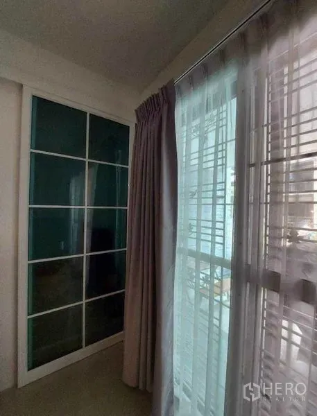 Townhouse for rent in Bang Phli, Samut Prakan - Bedroom corner with floor-to-ceiling curtains and sliding wardrobe with glass panels.
