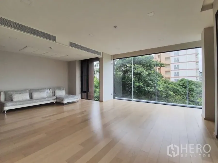 Condominium for sale in Huai Khwang, Bangkok - Spacious living room with floor-to-ceiling glass wall, light wood floors and leafy city views.