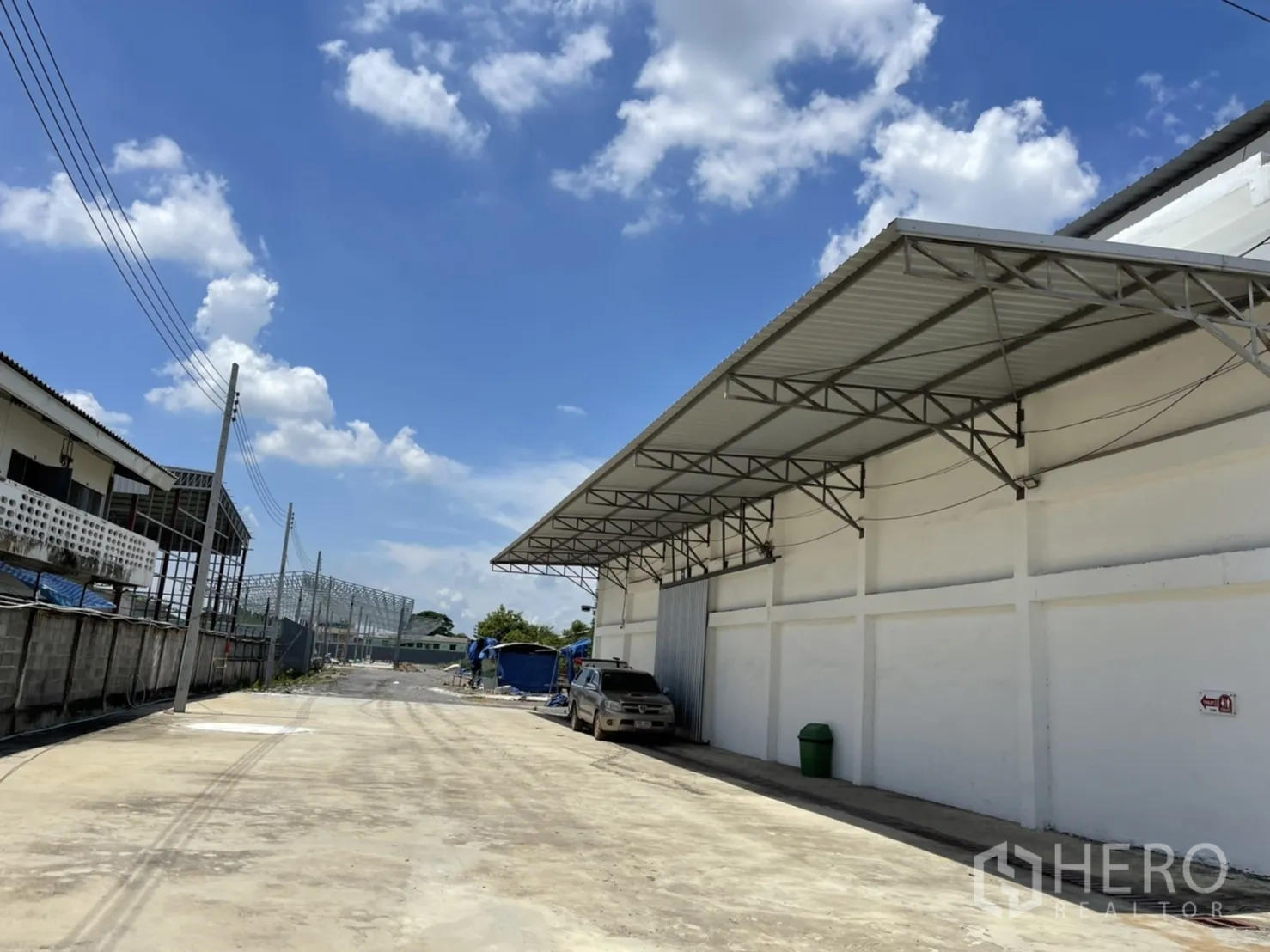 Warehouse for rent in Mueang Pathum Thani, Pathum Thani - Side lane beside the warehouse with long canopy, utility poles, and clear blue sky.