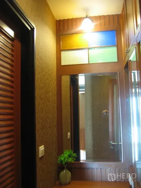 Condominium for rent in Khlong Toei, Bangkok - Compact hallway with a large mirror, stained-glass window panel and a wall sconce.
