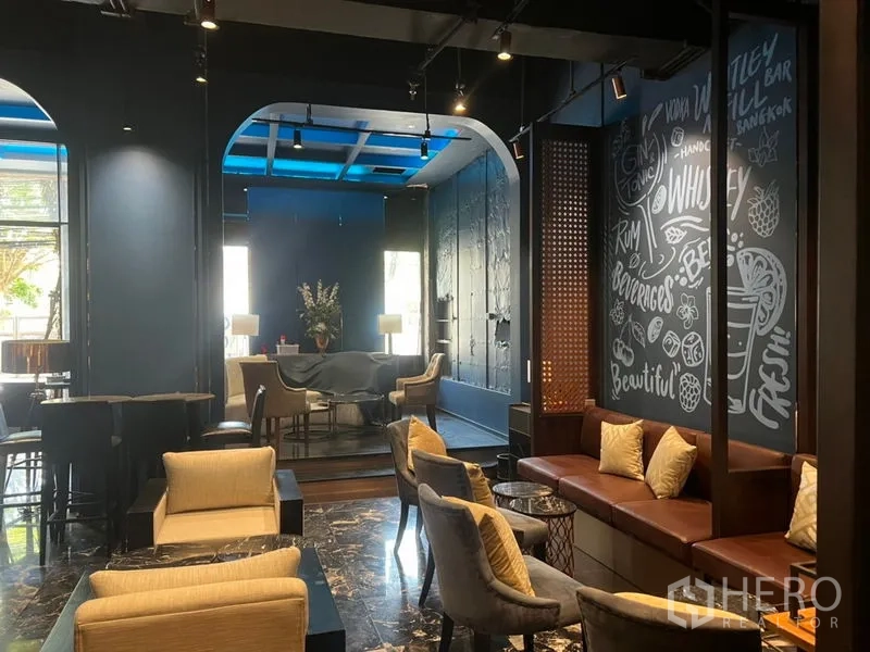 零售空间 出租在Watthana, Bangkok - 现代商铺内景，休闲区配大理石地面、拱形空间、手绘黑板墙及沙发与餐桌座椅。