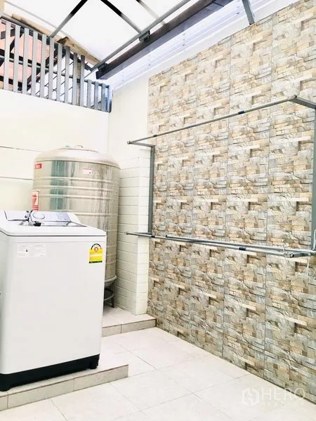 联排别墅 出租在Prawet, Bangkok - 带顶洗衣区，配洗衣机、不锈钢水塔与石纹墙面。