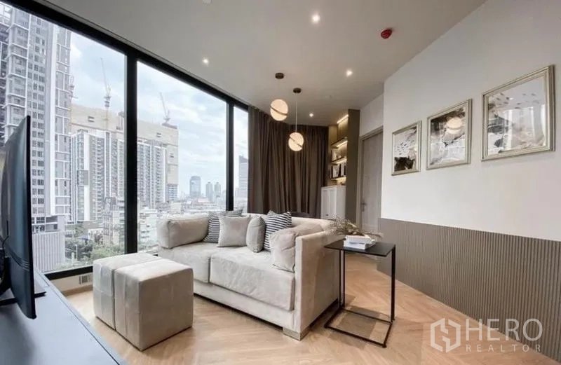 Condominium for rent in Din Daeng, Bangkok - Open living area with pendant lights, neutral décor and expansive windows overlooking Bangkok.