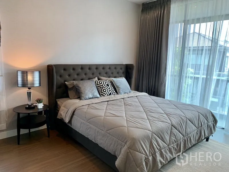 Detached House for rent in Bang Kapi, Bangkok - Cozy bedroom with tufted headboard, gray bedding, bedside table and full-height curtains.