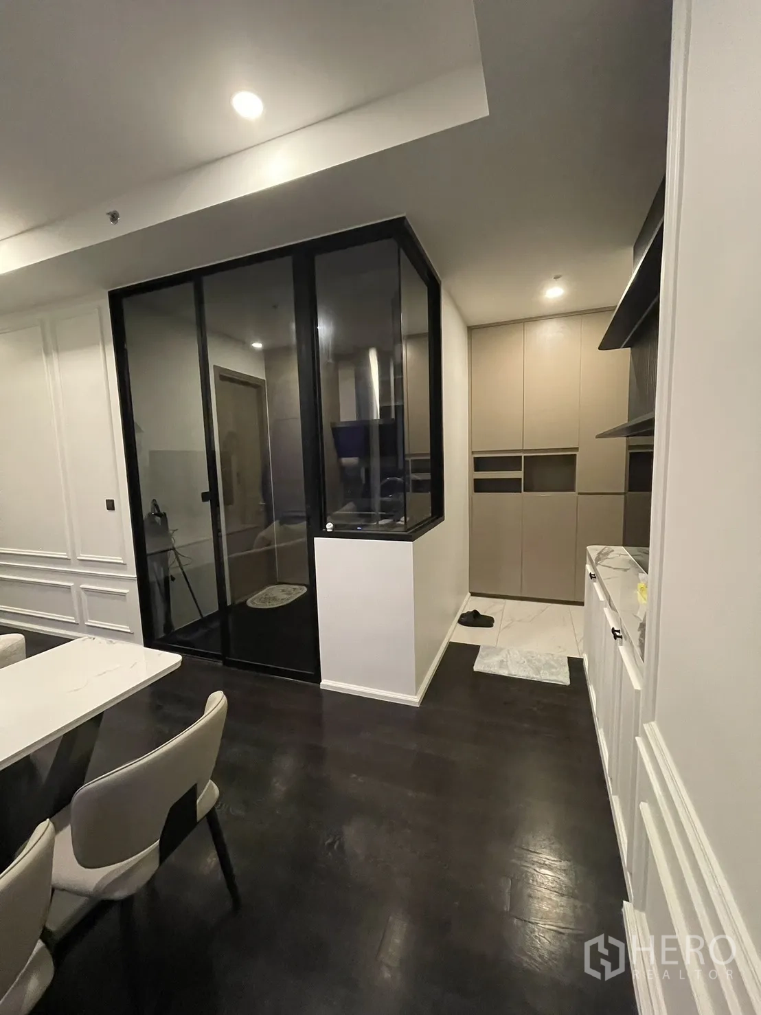Condominium for rent in Watthana, Bangkok - Living area beside a glass-partitioned kitchen and storage wall.