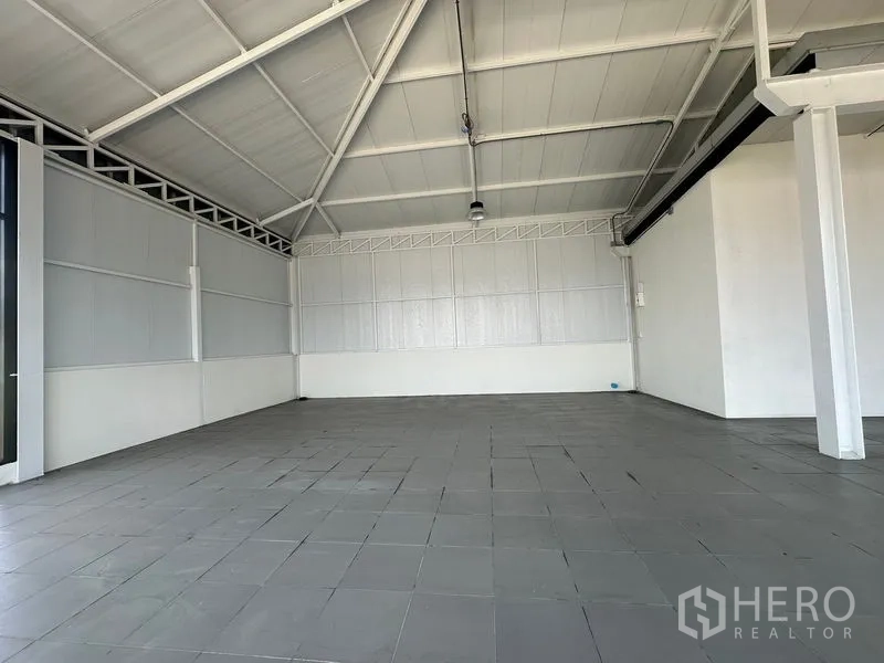 零售空间 出租在Bang Na, Bangkok - 空置店铺内景，白色墙板、外露屋梁、吊灯与灰色地砖。