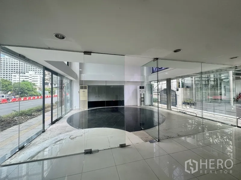 Retail Space for rent in Sathon, Bangkok - Bright double-height showroom with floor-to-ceiling windows and a circular black tile feature facing the street.