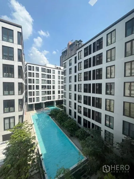 Condominium for rent in Watthana, Bangkok - Exterior of low-rise condominium buildings with a long central swimming pool surrounded by greenery.