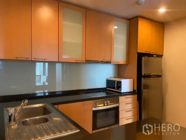 公寓 出租在Sathon, Bangkok - 开放式厨房，木质橱柜、黑色台面，配备嵌入式烤箱、炉灶、微波炉与双门冰箱。