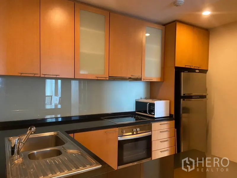 公寓 出租在Sathon, Bangkok - 开放式厨房，木质橱柜、黑色台面，配备嵌入式烤箱、炉灶、微波炉与双门冰箱。