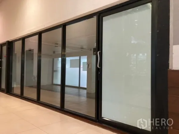 零售空间 出租在Khlong Toei, Bangkok - 曼谷艾卡迈室内走廊旁的商铺，黑色铝合金落地玻璃与滑动门。