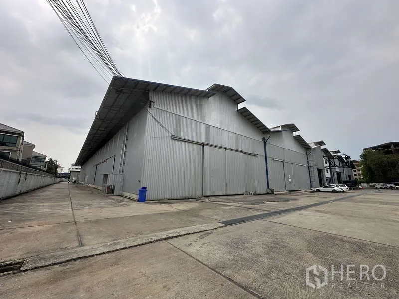 Warehouse for rent in Pak Kret, Nonthaburi - Exterior of a large corrugated steel warehouse with wide driveway and loading apron.