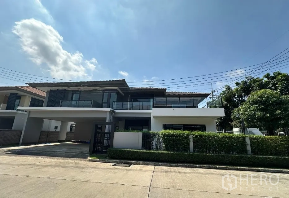 บ้าน ขายในLam Luk Ka, Pathum Thani - ภาพด้านหน้าบ้านกลางวัน มีแนวรั้วพุ่มไม้และที่จอดรถในร่ม