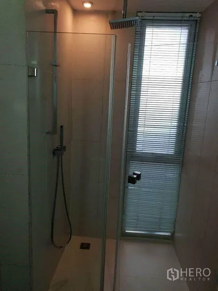 Condominium for sale in Bang Rak, Bangkok - Glass-enclosed shower with rain head next to a window with blinds.