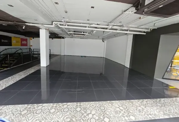 零售空间 出租在Bang Rak, Bangkok - 开放式零售铺面，黑色亮面地砖、白色墙面与裸露天花管线，旁有商场电动扶梯。