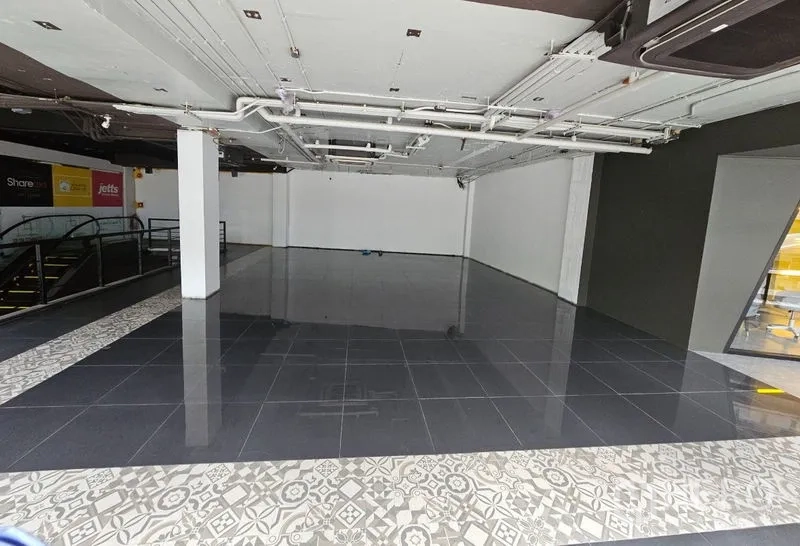 零售空间 出租在Bang Rak, Bangkok - 开放式零售铺面，黑色亮面地砖、白色墙面与裸露天花管线，旁有商场电动扶梯。