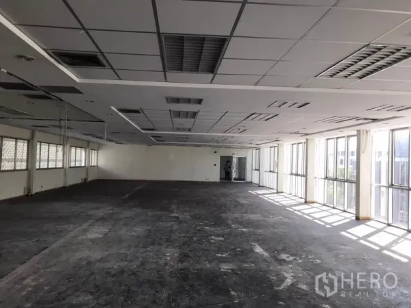 Office Space for rent in Khlong Toei, Bangkok - Large empty office space with ceiling lights, grid panels, and window walls leading to a doorway.