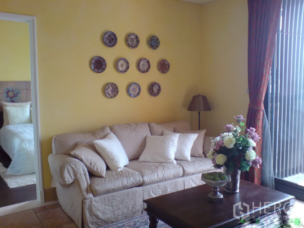 Condominium for rent in Khlong Toei, Bangkok - Cozy living room with beige sofa, wall plate art and floor-to-ceiling window.