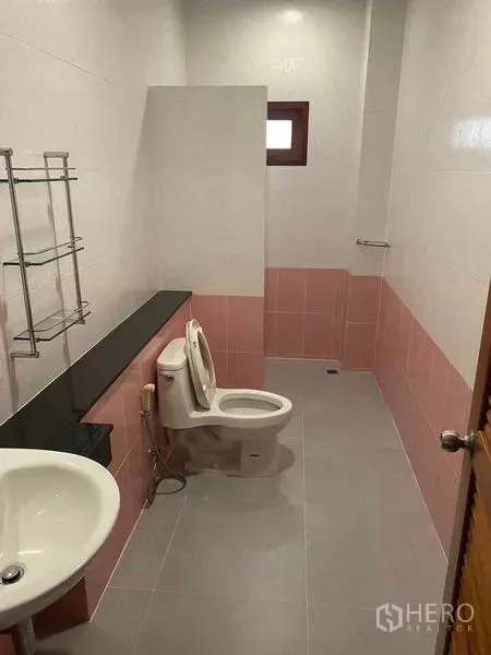Detached House for sale in Bang Khun Thian, Bangkok - Long bathroom with pink and white tiles, toilet, sink and a small window.