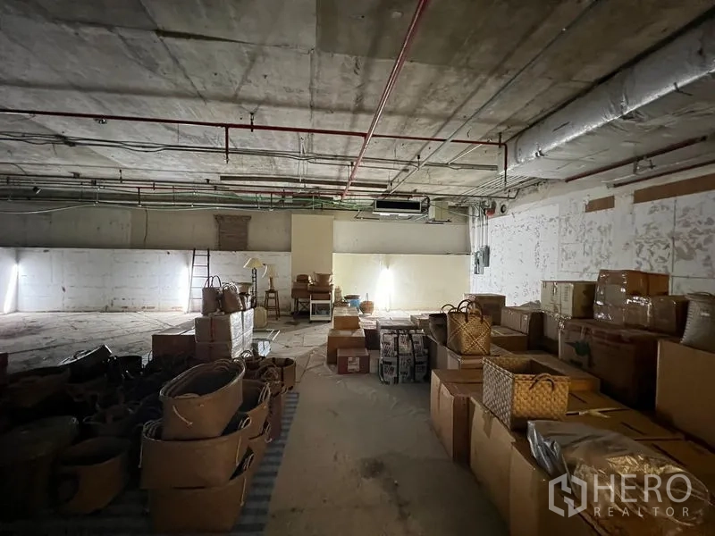 零售空间 出租 - 开放式室内，光线较暗，混凝土地面与成堆纸箱，处于装修前状态。