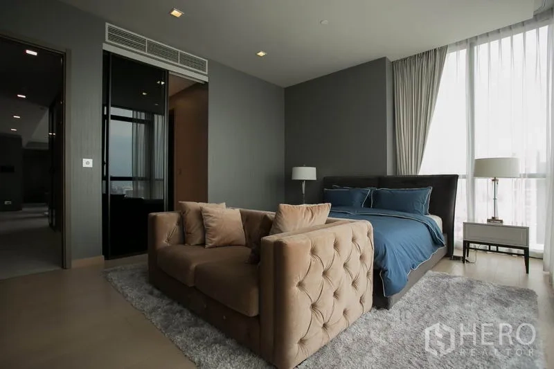 Condominium for rent or sale in Watthana, Bangkok - Spacious master bedroom with king bed, tufted sofa, bedside lamps and floor-to-ceiling windows.