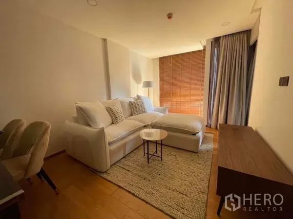 Condominium for sale in Pathum Wan, Bangkok - Living area with floor-to-ceiling curtains, soft lighting and access toward the balcony.