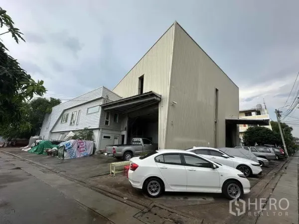 Home Office for rent in Bang Khen, Nonthaburi - High-bay warehouse and office exterior with multiple parked cars along a concrete driveway.