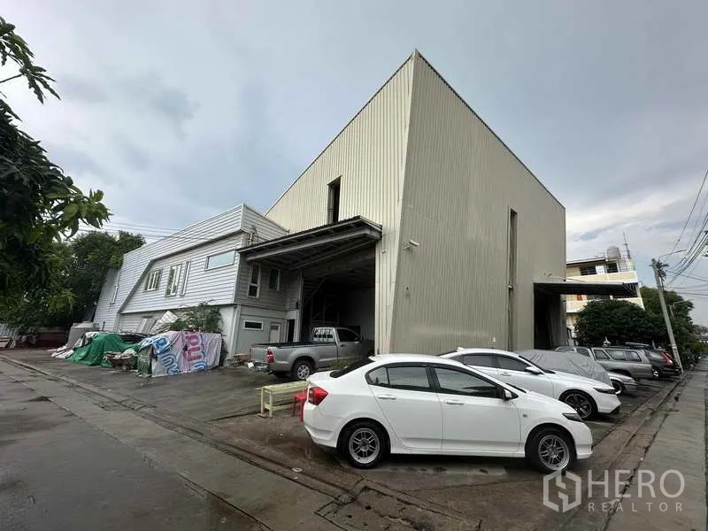 Home Office for rent in Bang Khen, Nonthaburi - High-bay warehouse and office exterior with multiple parked cars along a concrete driveway.