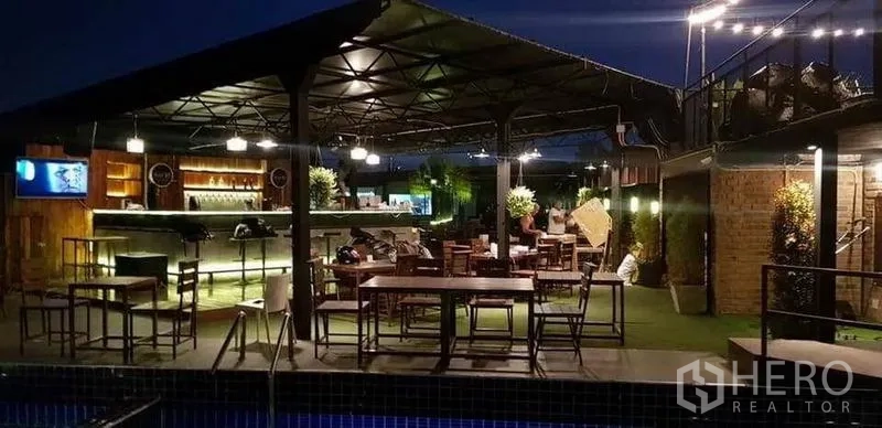零售空间 出租在Khlong Toei, Bangkok - 泳池畔酒吧与用餐区，夜间照明温暖。