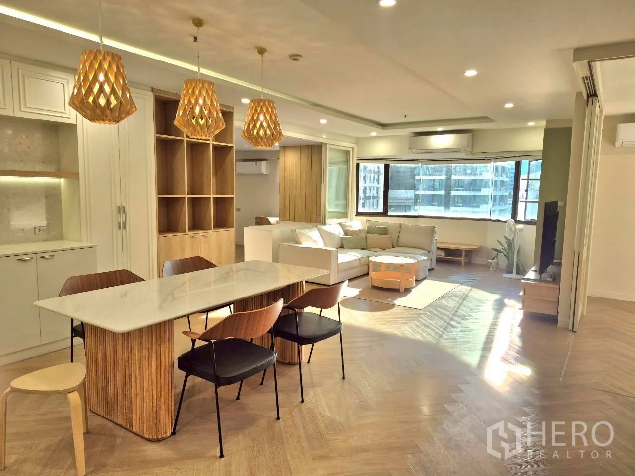 公寓 for rent in Watthana, Bangkok - 明亮的开放式客餐厅，转角沙发、石材餐桌、木质吊灯、内置收纳、人字拼地板与大窗景观。