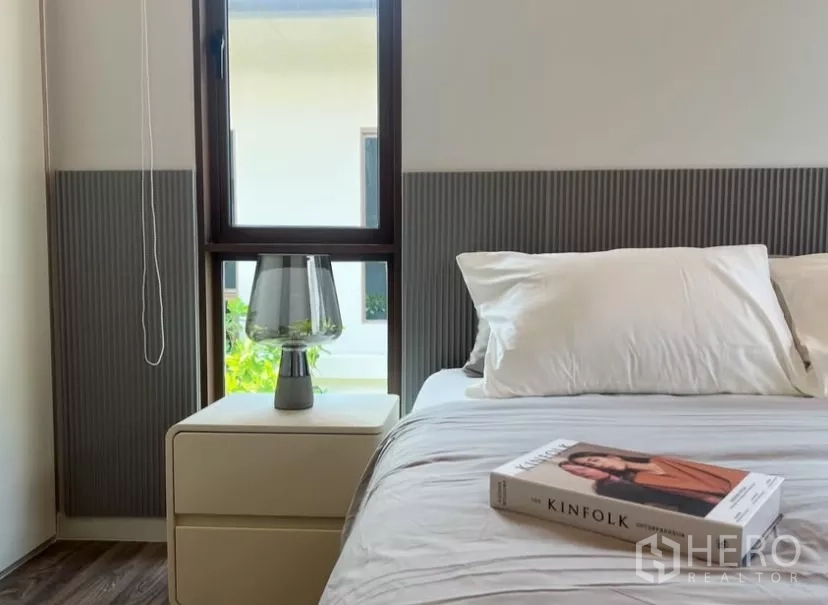 Detached House for rent or sale in Bang Kapi, Bangkok - Secondary bedroom with bedside table, lamp, and garden-view window.