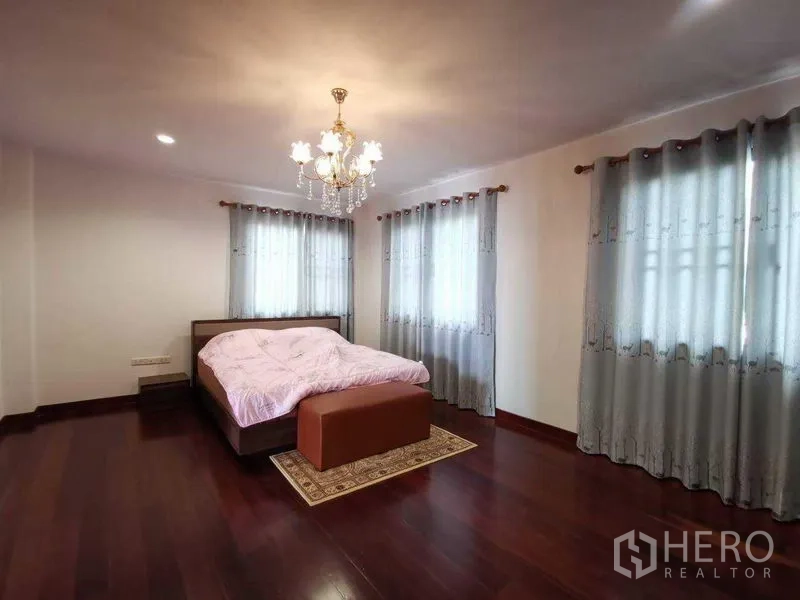 Detached House for rent in Prawet, Bangkok - Bright bedroom with chandelier, corner windows with grey drapes, hardwood floors and bed bench.