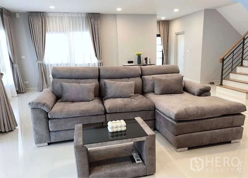 Detached House for rent in Bang Phli, Samut Prakan - Open-plan living room with large grey L-shaped sofa and staircase in the background