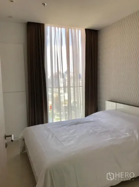 Condominium for rent or sale in Pathum Wan, Bangkok - Cozy bedroom with patterned wallpaper, sheer and blackout curtains, and a city view.